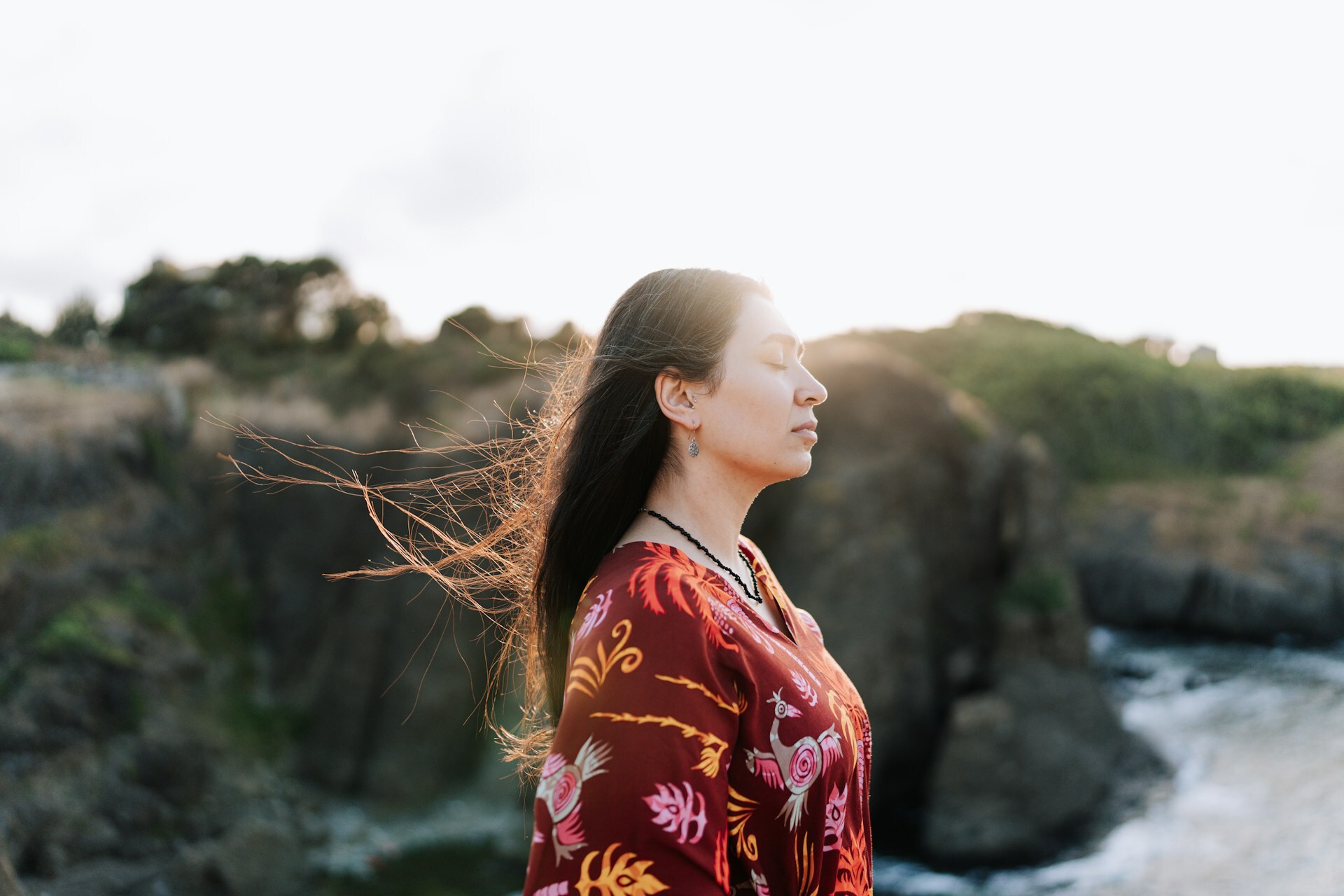 A woman with her eyes closed, contemplating in front of a body of water