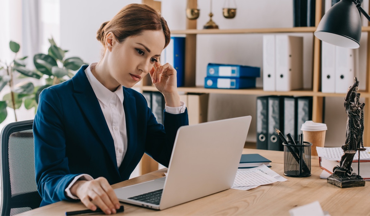 Female lawyer in suit working on laptop at workplace in office.